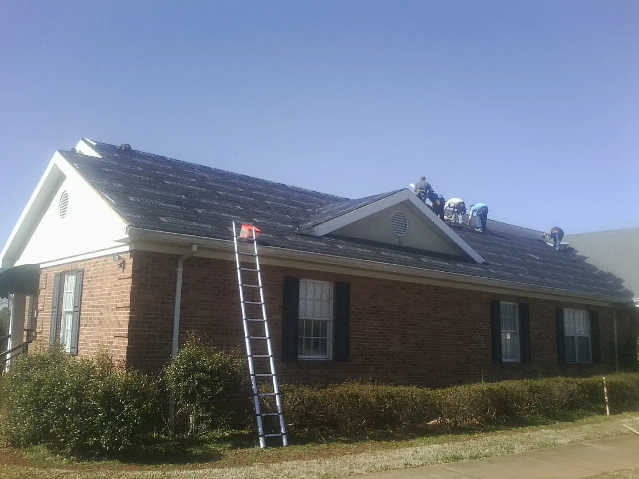 Crew tearing shingles off a brick ranch roof with a ladder set — Metal Roof Repair work by our crew in Castalian Springs