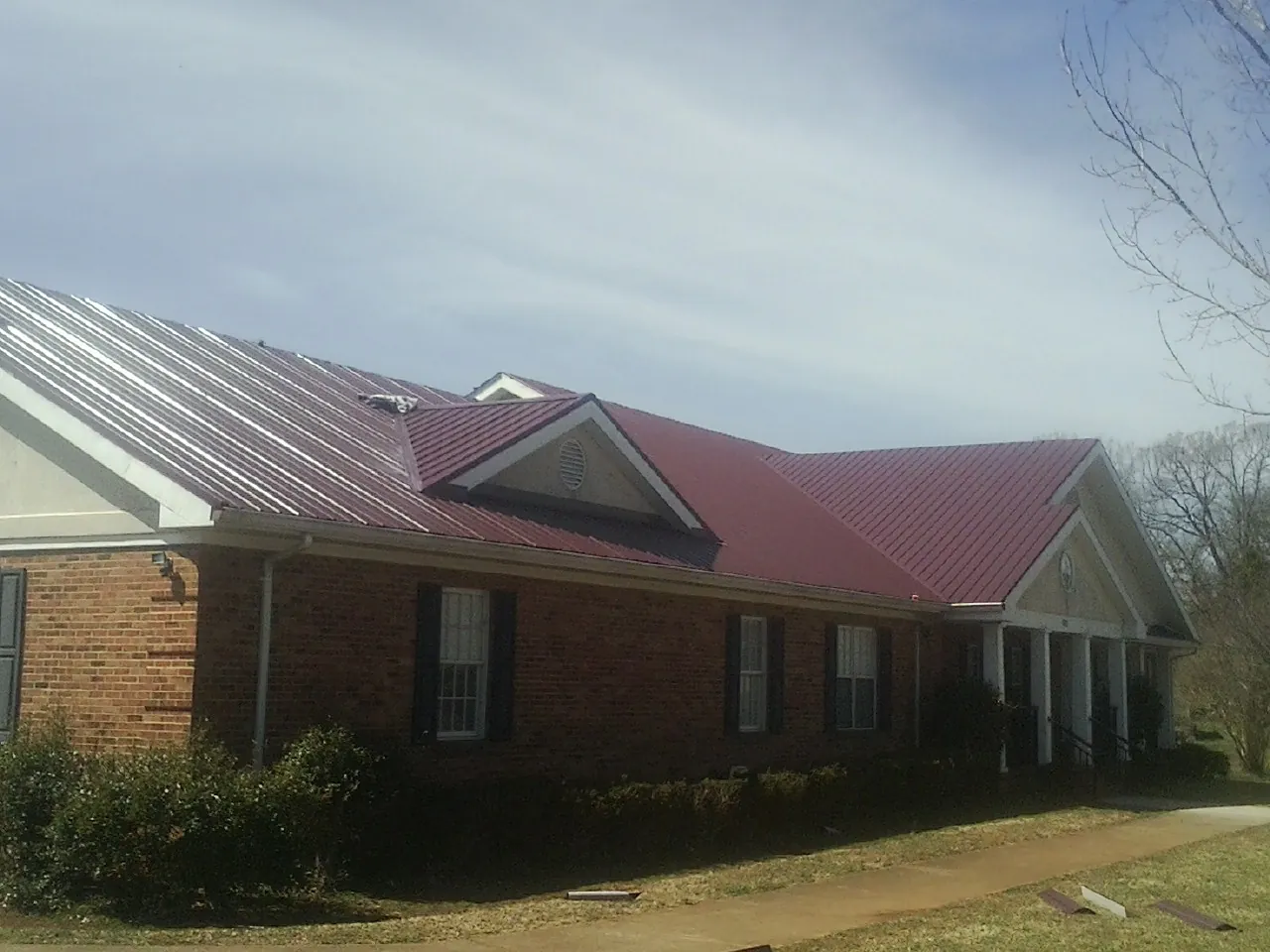 Red metal roof with gabled entries on a long brick building, from a Hail Damage Roof Repair job in Castalian Springs