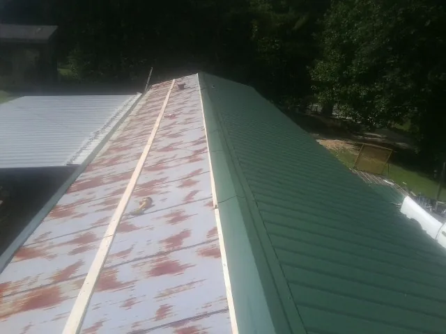 Old rusted panels beside newly installed green metal roofing — Wind Damage Roof Repair by Roofing Brothers in Castalian Springs