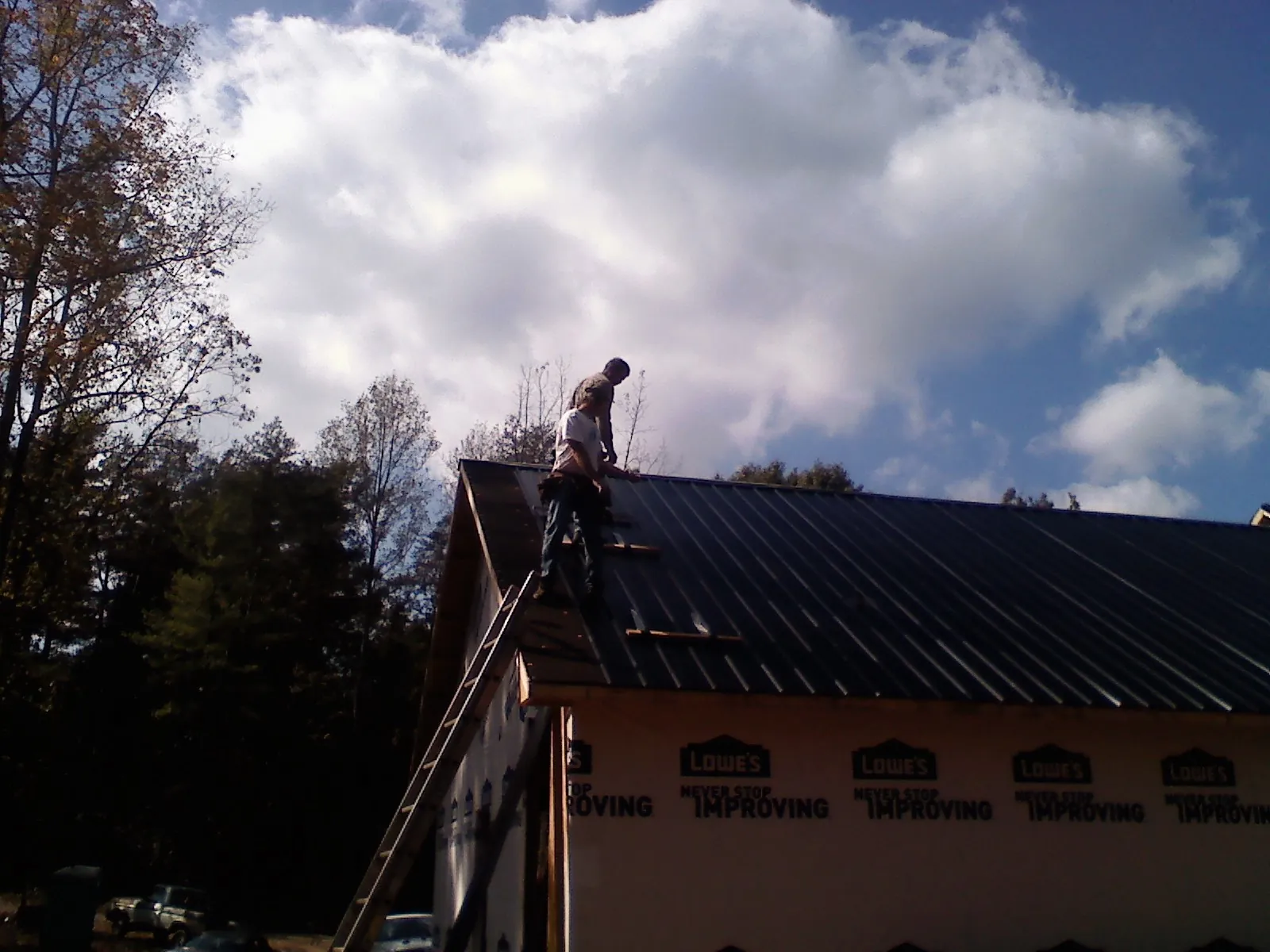 Roofer fastening dark metal panels high against a cloudy sky, from a Roof Inspection job in Castalian Springs