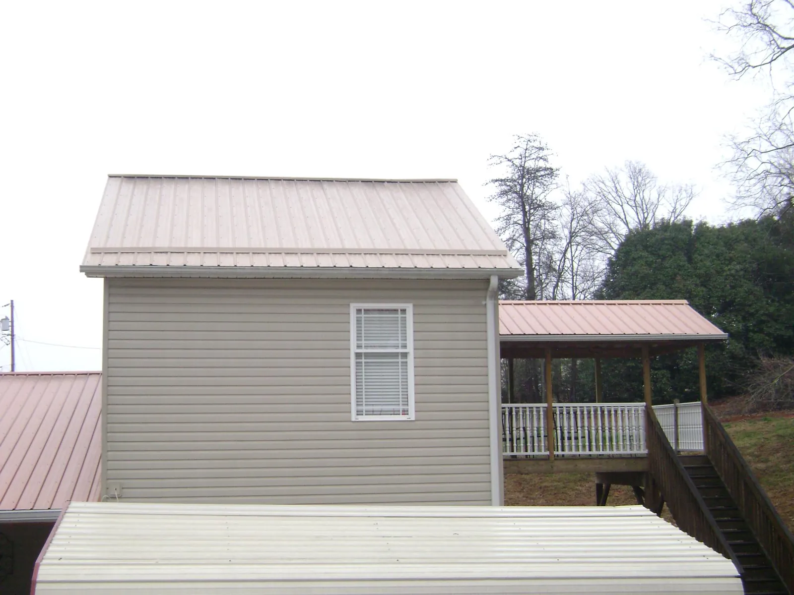 Tan metal roofs on a two story addition and attached porch, from a Roof Replacement job in Castalian Springs